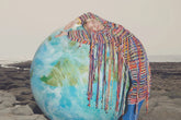 Person wrapped in colorful fabric standing next to a globe on a rocky surface
